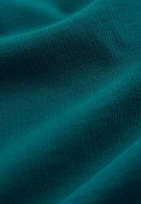 Teal színű szövet, sima, texturált felülettel és finom bordázattal, amelyen finom szín- és fényváltozások láthatók.