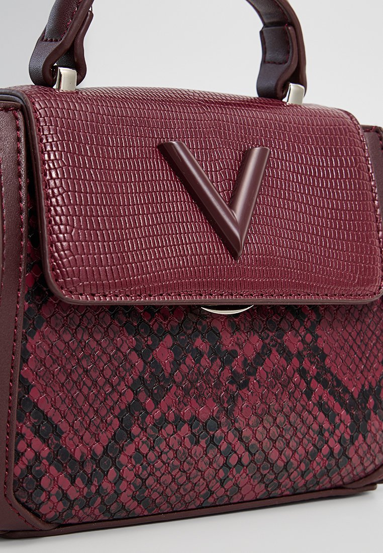 Sac à main en bordeaux avec un dessus texturé et un motif serpent à l'avant. Comprend un accent en forme de V proéminent et une quincaillerie en argent.