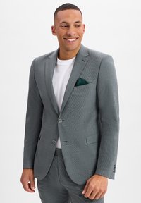 Szary marynarka o fakturowanej powierzchni z klapami typu notch, na dwa guziki i z chusteczką w kieszeni. Noszona na białym t-shircie, w zestawie z dopasowanymi spodniami.