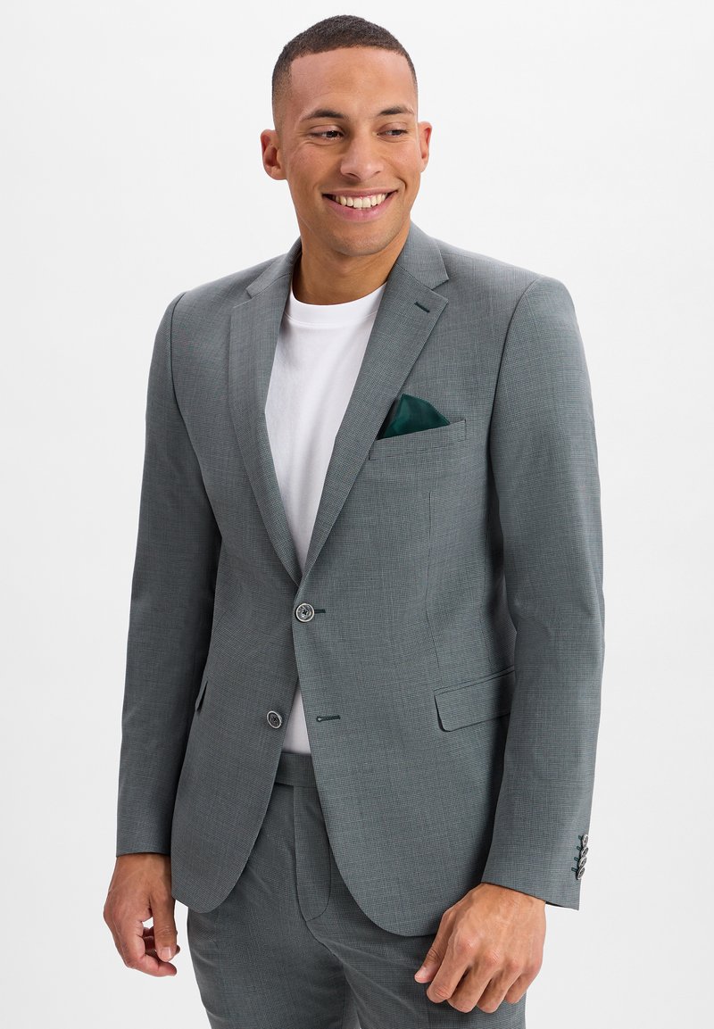 Grijs structuur blazer met notch revers, twee knopen en een pochet. Draagt over een wit T-shirt, gecombineerd met bijpassende broek.