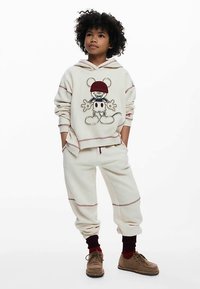 Kermanvärinen huppari kirjotulla hahmolla, raidallisilla yksityiskohdilla, yhteensopivat collegehousut ja ruskeat nauhalliset kengät. Rentoa ja mukavaa designia.