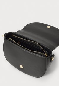 Svart lær crossbody-veske med en buet form, gulldetaljer og et glidelåslukket interiør med flere rom.