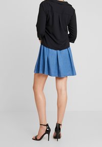 Blusa nera con maniche a tre quarti e colletto, abbinata a una gonna di jeans.Tacchi neri trasparenti completano l'outfit.