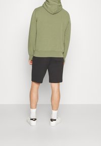 Grön huvtröja, svarta shorts, vita sneakers med svarta detaljer och vita strumpor. Fitted design med en mjuk textur. Avslappnad klädsel.