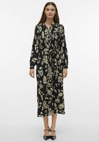 Robe longue noire avec un motif floral crème, col, manches longues, taille cintrée avec lien, et longueur mi-mollet fluide.