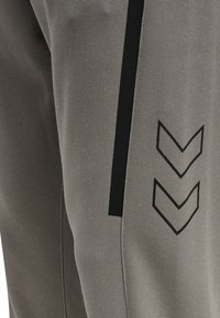 Grå sportbukser med et struktureret stof, slim fit og sorte accentstriber med chevronmønstre på siden.