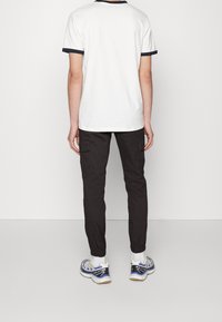 Biała bawełniana koszulka z granatowym wykończeniem, w zestawie z czarnymi spodniami cargo z bocznymi kieszeniami oraz szaro-niebieskimi butami sportowymi.