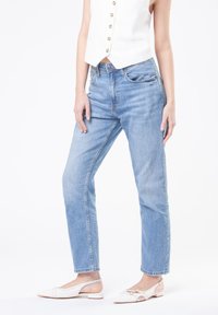 Jeans in denim leggero azzurro con una vestibilità a gamba dritta, caratterizzati da un alto punto vita e un leggero effetto invecchiato. Abbinati a scarpe bianche senza lacci.