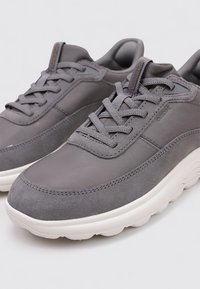 Baskets grises en cuir lisse et en daim, avec un bout arrondi, une languette texturée et une épaisse semelle en caoutchouc blanc avec un logo discret.