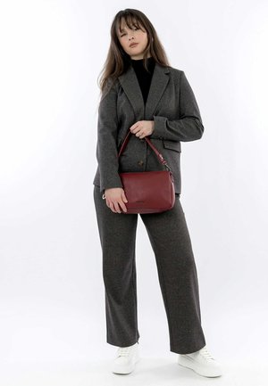 Completo in misto lana grigio con blazer su misura e pantaloni a gamba larga. Tiene una piccola borsa di pelle rossa. Sneakers bianche completano l'outfit.