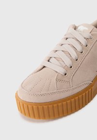 Beige semsket sneakers med tykk gummisåle, beige flate lisser og en liten isbjørnlogo på tungen.