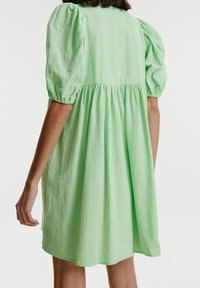 Robe à manches courtes, longueur genoux, en tissu vert clair avec taille froncée et manches bouffantes douces, présentant une silhouette fluide et décontractée.