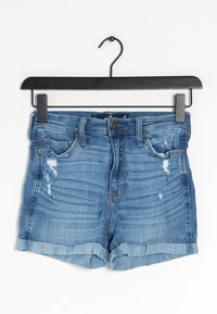 Jeansshorts med ljusblå tvätt, slitna detaljer, uppvikta fållar och femfickdesign, hängande på en svart galge.