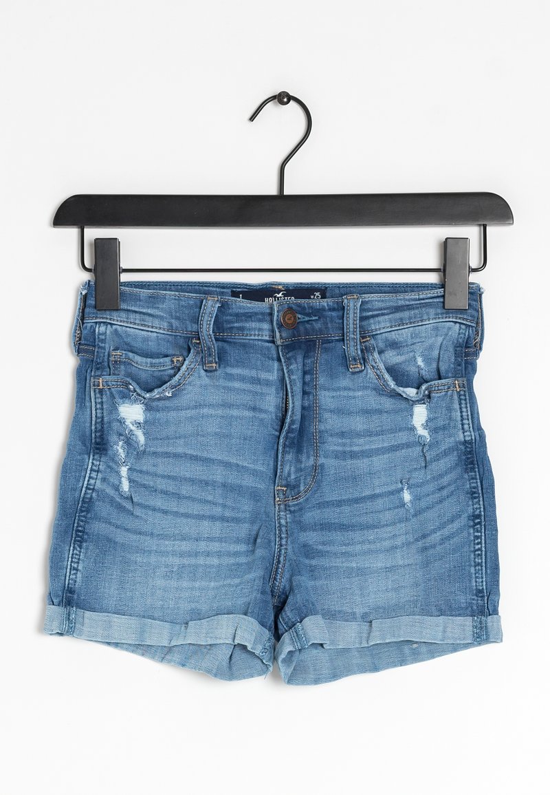 Shorts en denim avec un délavage bleu clair, des accents déchirés, des ourlets retournés et un design à cinq poches, suspendus sur un cintre noir.