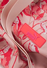 Sac floral rose en tissu lisse, orné de motifs de fleurs rouges et blanches. Comprend un patch rectangulaire Puma lumineux en rose.