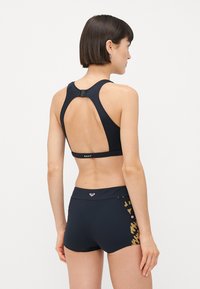 Black sports bra with a racerback design, featuring a clasp at the back. Paired with black shorts adorned with a gold and pink patterned accent.