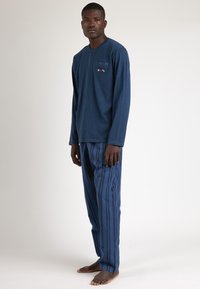 Top de manga larga navy con detalles de botones, combinado con pantalones a rayas azules. Tejido suave con un corte relajado. Sin zapatos.