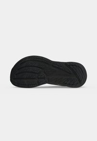 Semelle de chaussure en caoutchouc noir avec des motifs de bande de roulement texturés pour l'adhérence et la durabilité, présentée sur un fond blanc uni.