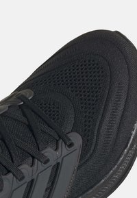 Gros plan sur une chaussure de sport noire montrant un mesh respirant texturé, les lacets et une partie de la semelle en caoutchouc.