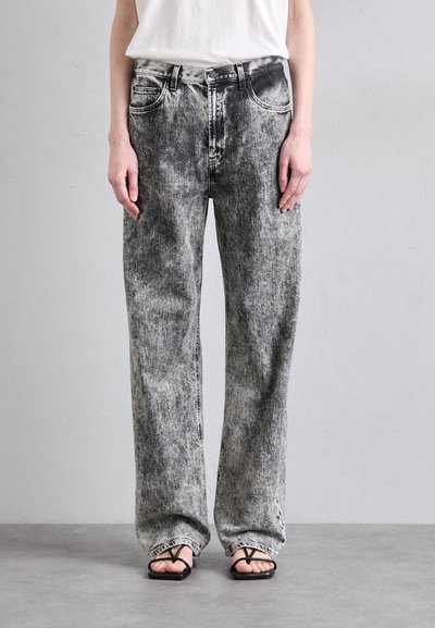 Højtaljede, brede ben sorte og grå marmorjeans med forlommer, kontrastsyninger og knaplukning. Flade sandaler bæres.