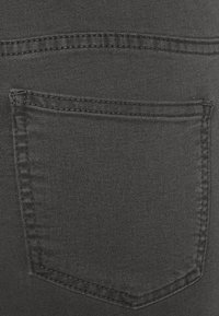 Svart denimtyg har en bakficka med synlig söm. Texturen är slät med en lätt lyster och minimal blekning.