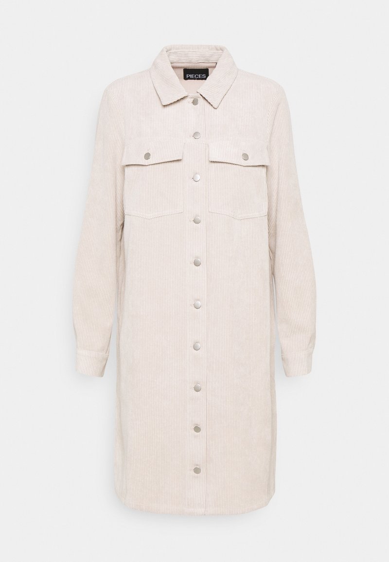 Robe-chemise en velours côtelé beige avec col, manches longues, deux poches poitrine et fermetures à boutons argentés sur le devant. Texture côtelée verticale.