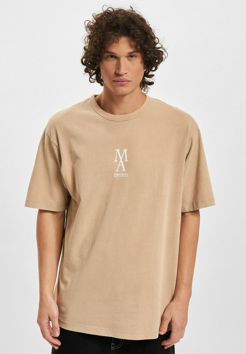 Beige bomull T-skjorte med korte ermer, rund hals og en liten hvit logo på brystet. Enkel, avslappet passform.
