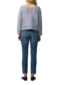 Helles lilafarbenes, offen gestricktes Sweater mit einem cropped Schnitt und langen Ärmeln, kombiniert mit mitteltiefblauen Skinny-Jeans mit fransigen Säumen und Gesäßtaschen.