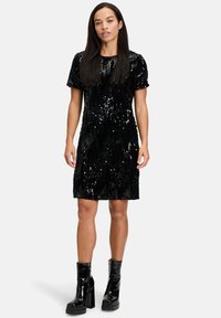 Czarna sukienka z cekinami, z krótkimi rękawami, okrągłym dekoltem, prostym krojem i błyszczącą powierzchnią. Połączona z błyszczącymi czarnymi botkami na platformie.