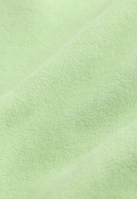 Tissu vert clair avec un tricot fin et texturé. Surface douce et lisse, pliée pour montrer la profondeur et la tenue du matériau.