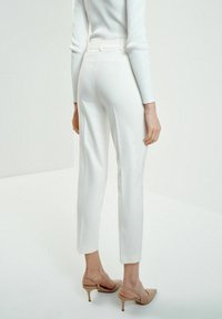 Białe dopasowane spodnie o długości do kostek, wykonane z gładkiego materiału; zestawione z jasnobeżowymi butami na obcasie typu slingback.