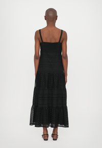 Rochie maxi din dantelă neagră, cu bretele subțiri ajustabile, design în straturi și o parte superioară texturată. Prezintă un tiv volănat.