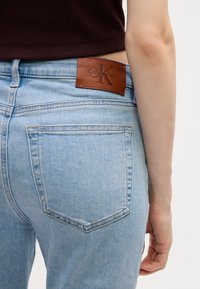Svetlomodré džínsy s priliehavým strihom, s koženým štítkom Calvin Klein na zadnom páse a štandardnými zadnými vreckami.