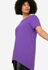 Paarse t-shirt met korte mouwen, een relaxte pasvorm, ronde halslijn en een asymmetrische zoom, gecombineerd met zwarte legging.