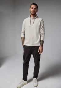 Sudadera con capucha gris claro de manga larga con cordones, combinada con pantalones cargo oscuros con bolsillos laterales y zapatillas blanco.