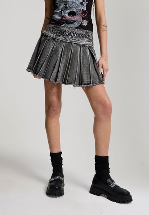 Mujer con una minifalda negra plisada de mezclilla con rosas bordadas, una camiseta con gráfico de dragón, calcetines negros y zapatos de plataforma negros.