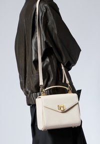 Sac à main en cuir imprimé crocodile crème avec une poignée supérieure, une bandoulière amovible et des accents en métal doré.