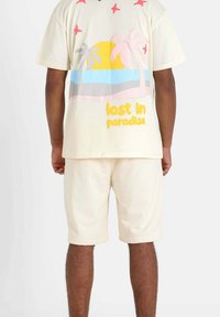 Cream short-sleeve shirt with colorful palm tree and sun graphic on the back, paired with matching cream shorts. Cotton material, relaxed fit.