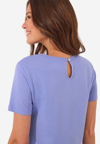 T-shirt in cotone lavanda a maniche corte con apertura a chiave sul retro chiusa da un piccolo bottone. Tessuto liscio con vestibilità rilassata.