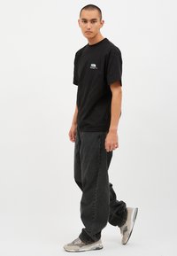 Musta puuvillapaita, jossa on pyöreä kaula-aukko, lyhyet hihat ja värikäs graafinen kuva rintamalla. Yhdistetty tummiin farkkuihin ja vaaleisiin lenkkareihin.