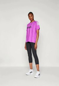 Paarse sportt-shirt met wit adidas-logo, korte mouwen en strepen; gecombineerd met zwarte leggings en witte sneakers.