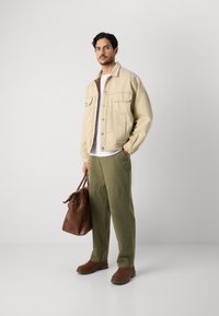 Khaki denim jacket, white t-shirt, olive green pants, brown leather shoes, and a brown leather bag. Notable details include buttoned pockets.