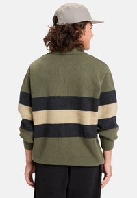 Zeleni pulover s crnim i kremastim prugama, mekanog tekstura, oversized kroj, rebrasti rukavi, pogled sa leđa, minimalistički dizajn.