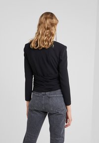 Haut noir à manches longues avec un détail froncé à l'arrière, associé à un jean gris taille haute présentant une texture classique en denim et des poches.