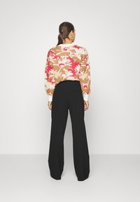 Maglione a maglia con motivo floreale nei colori rosa, bianco e marrone; abbinato a pantaloni neri a vita alta e gamba larga. Modello visibile da dietro.