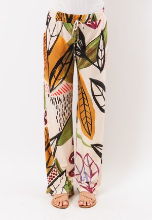 Pantaloni larghi con motivi astratti di foglie e geometrie in arancione, verde, nero, rosso e viola, indossati con sandali beige.