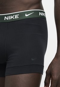 Gros plan d'une personne portant un boxer noir Nike avec une ceinture vert foncé arborant le logo Nike blanc et le swoosh.