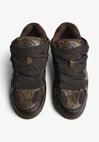 Sötétbarna tornacipő pár vastag, texturált fűzőkkel és műbőr kígyóbőr mintázattal a felsőrészén, fehér háttéren, felülről nézve.