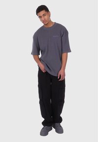T-shirt gris oversize à manches courtes avec un motif texturé, associé à un pantalon cargo noir avec des poches latérales et des baskets grises.
