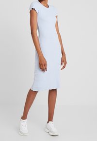 Vaaleansininen poimutettu midimekko, jossa on lyhyet röyhelöhihat, tekstuurilla varustettu kangas ja rispaantunut helma. Yhdistetty valkoisiin lenkkareihin.